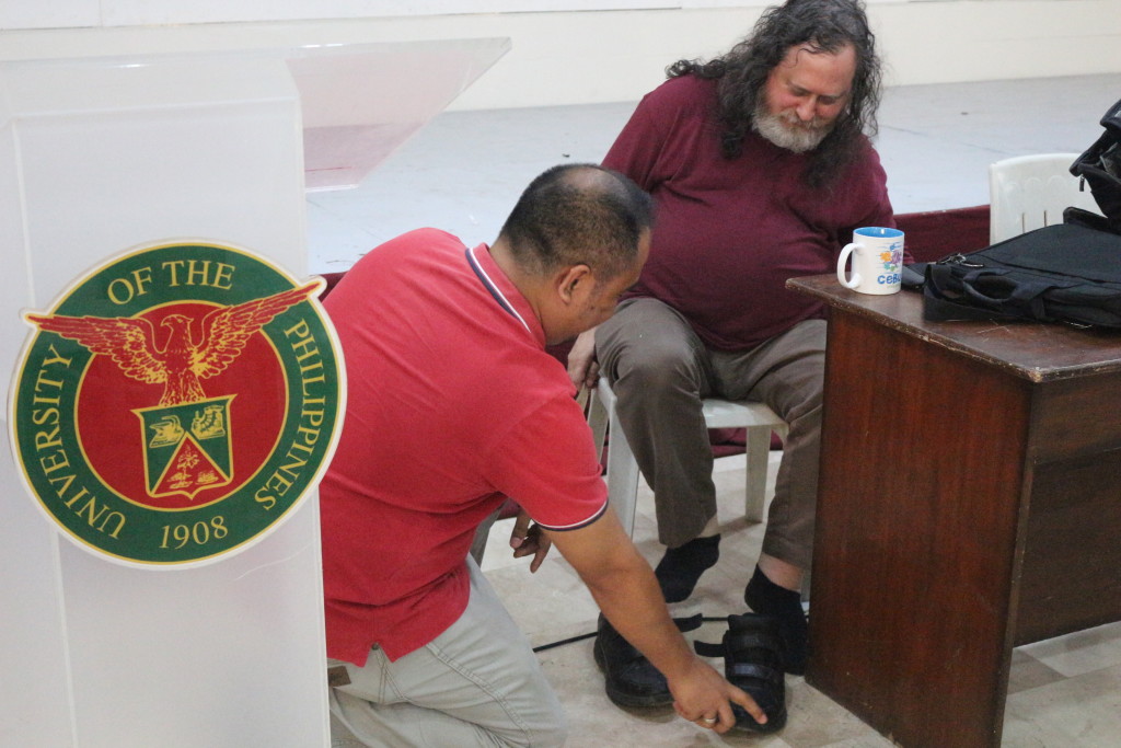Richard Stallman putting back his shoes on with a little help from Jerome Auza.